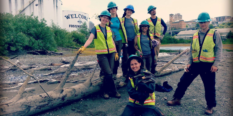 EarthCorps alum, Lindsey Falkenburg with a group of corps members, wearing hard hats and safety vests.