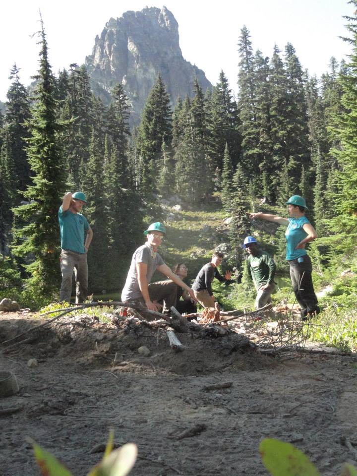 Six corps members at work in the field with trees and a mountain in the background