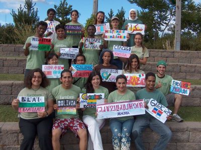 A group of international Corps Members all sitting together holding signs that share where each person is from