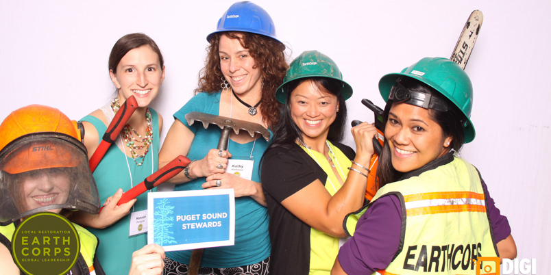 Clarissa Bulosan with other Puget Sound Stewards smiling in a photo booth, while holding tools and wearing hardhats.