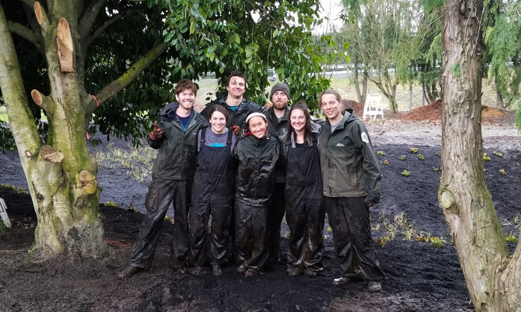 Corps Members in waders smiling in front of the rain garden.