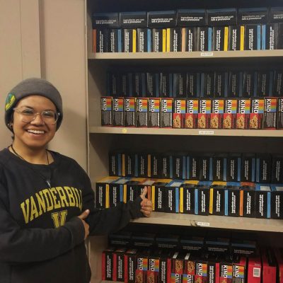 Person smiling and giving the thumbs up, next to shelves of KIND bars. 