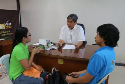 A man behind a desk talking with two young people.