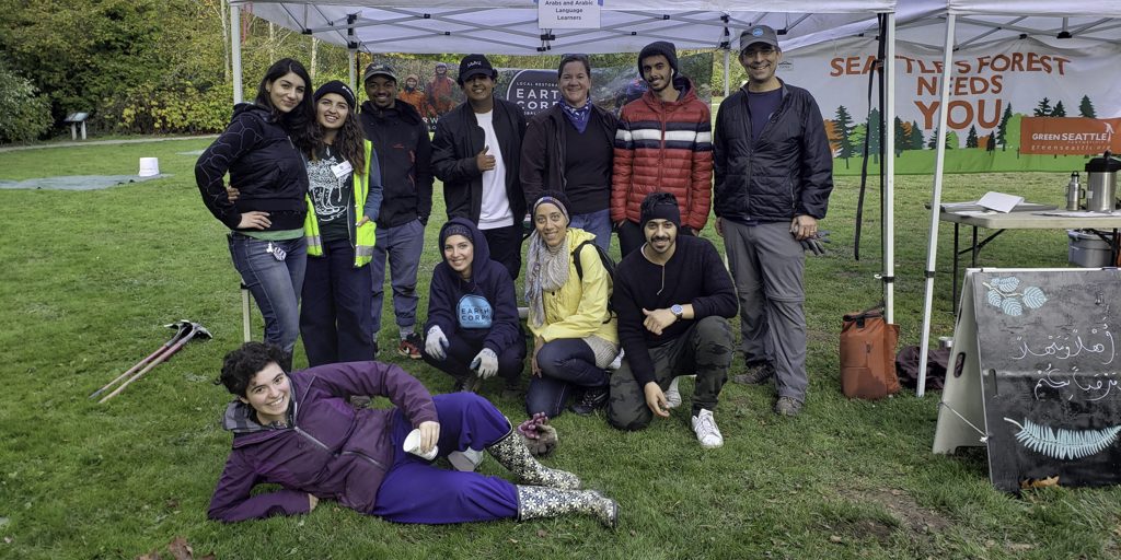 Volunteer Specialist, Nebras Maslamani and Executive Director Steve Dubiel, with a group of people smiling in front of a white tent in a grassy field.