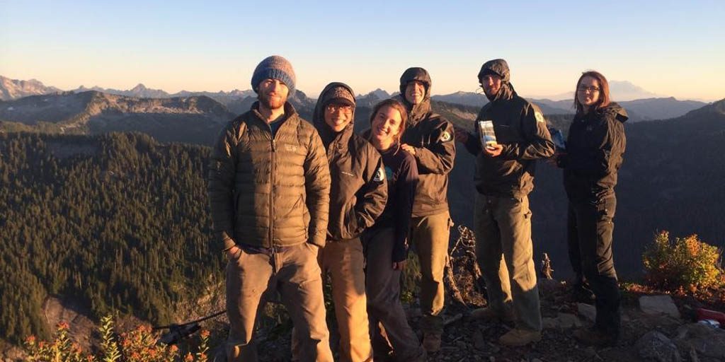 EarthCorps alum, Nicole Marcotte smiling with a group of Corps Members in front of a mountain landscape.