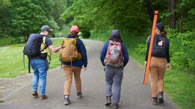 Four EarthCorps crew members walking with their gear down a paved park path.
