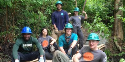 EarthCorps alum, Nicole Marcotte with a group of Corps Members smiling and wearing hard hats in a forested area.