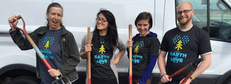 Four smiling volunteers standing in front of a white van, holding tools. 