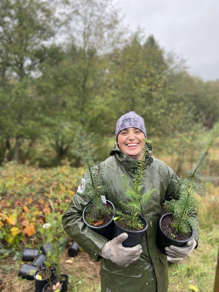 Volunteer specialist, Fernando Silveira holding three potted plants in a forested area. 