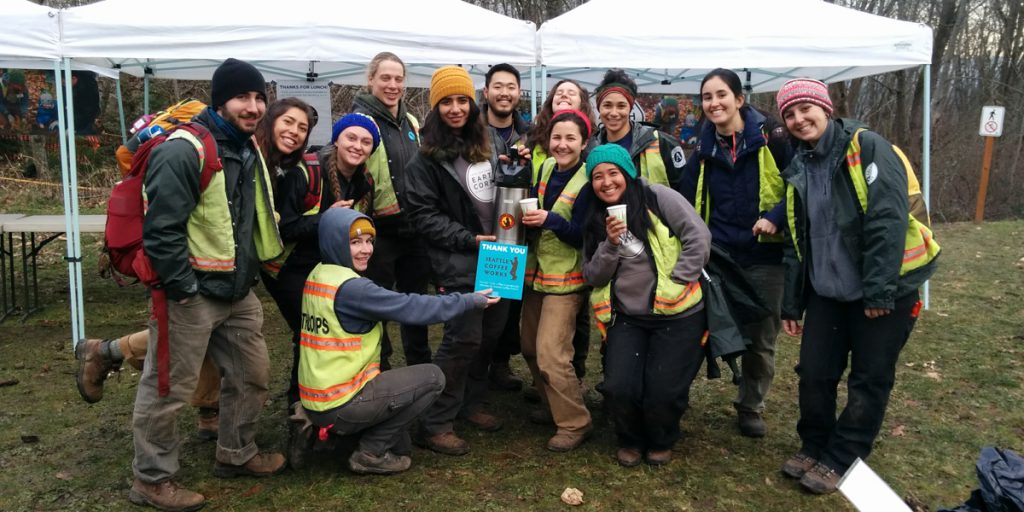 A group of EarthCorps volunteer specialists, wearing safety vests, smiling in front of a white tents outside. 