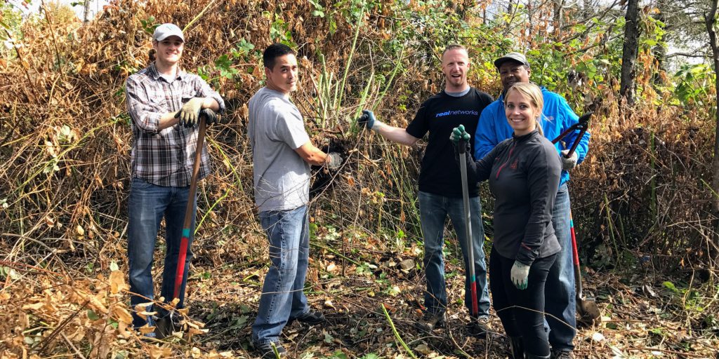 Small group of EarthCorps volunteers outside, smiling and holding tools.