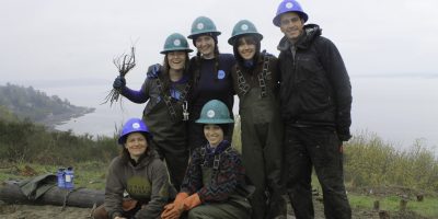 Project manager, Madeline de Mahy and Corps Members smiling and wearing hard hats.