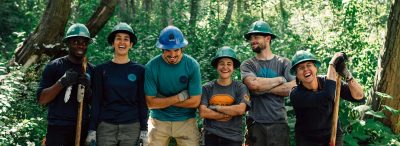 Group of smiling and laughing Corps Members wearing hard hats.