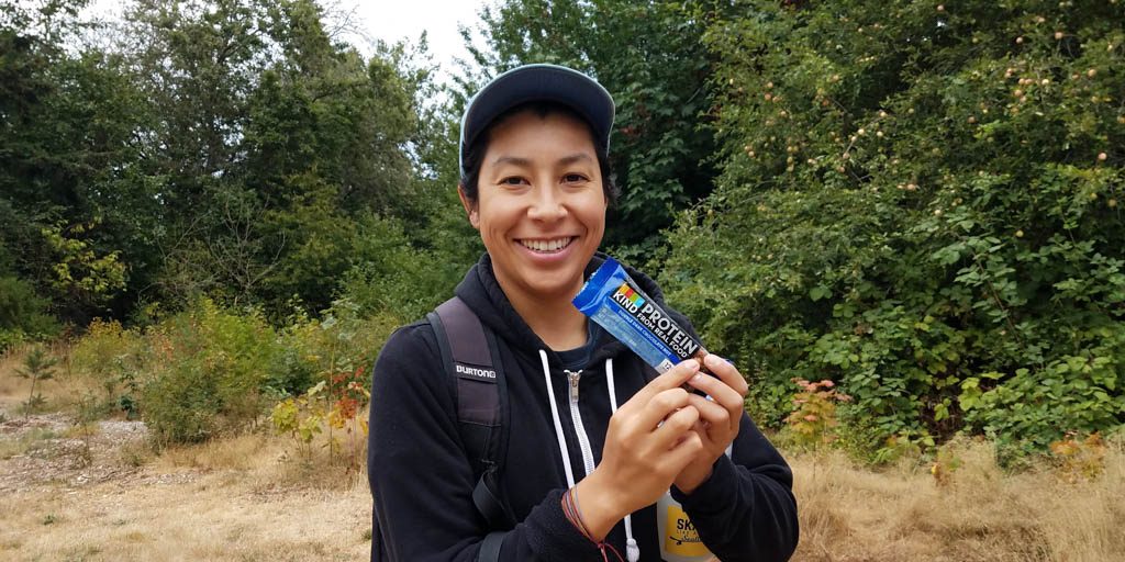 A person smiling and holding up a KIND protein bar.