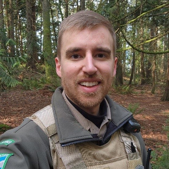 WA Parks Ranger Kyle Christensen smiling at the camera while standing in the forest.