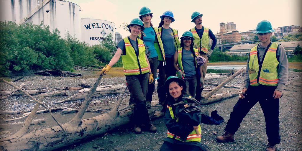 EarthCorps alum, Lindsey Falkenburg with a group of corps members, wearing hard hats and safety vests.