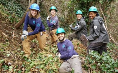 EarthCorps alum, Tom Lawler, and Corps Members wearing hardhats, smiling next to a pile of ivy that had been removed.