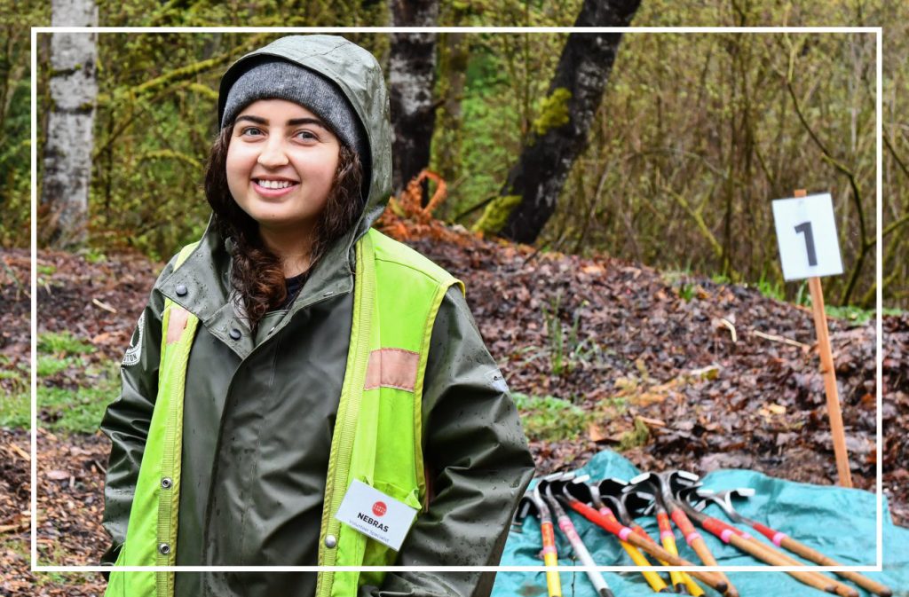 EarthCorps Volunteer Specialist, Nebras Maslamani smiling while wearing a safety vest and raincoat.
