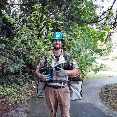 Smiling Corps Member wearing a hard hat and holding plants.