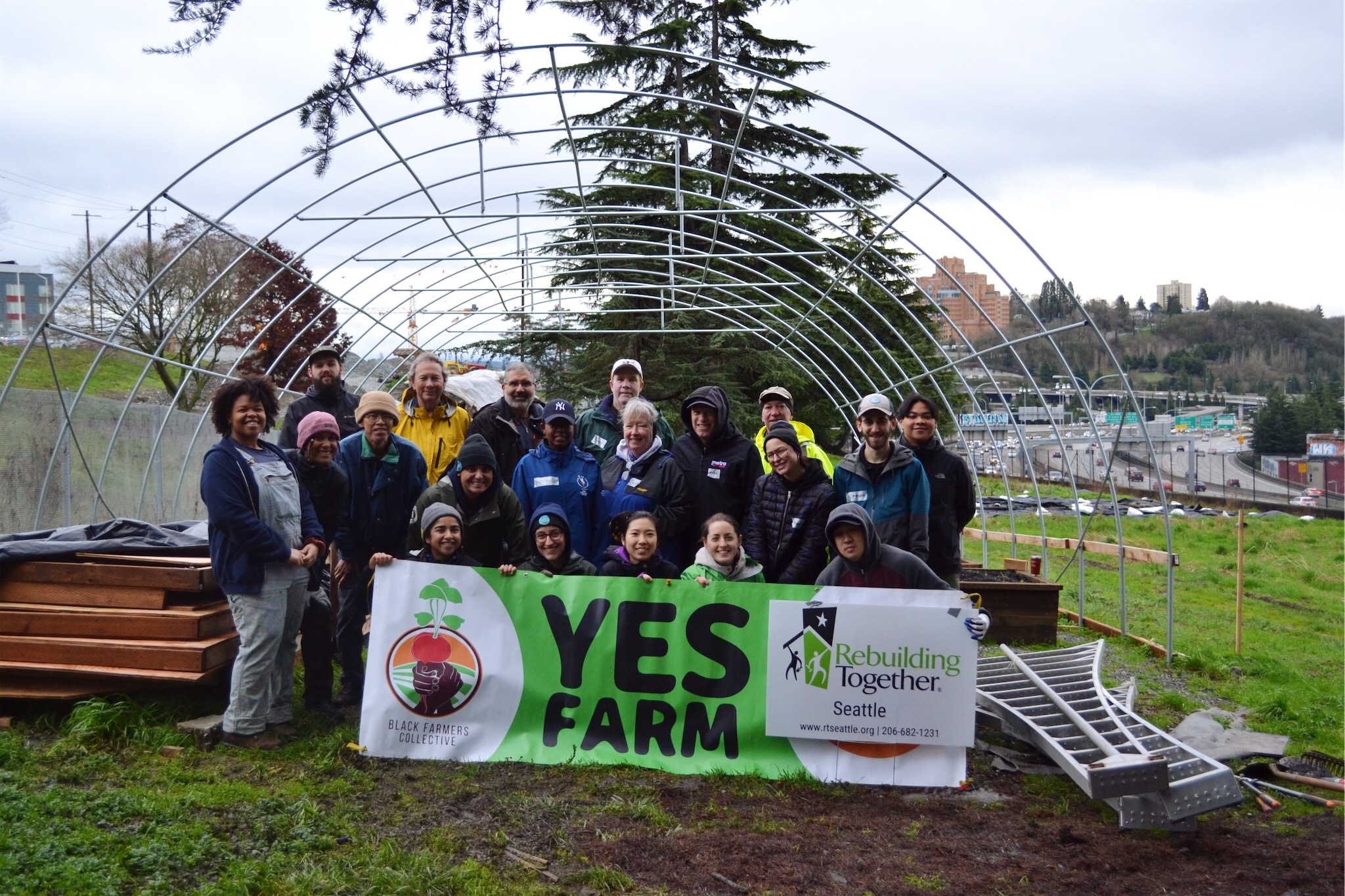 A group of smiling people in greenspace surrounded by the city, holding up a large Yes Farm sign.