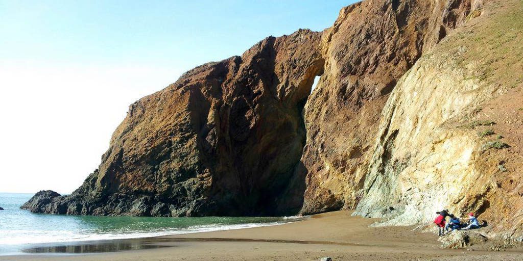 Three people on a beach next to a large rock formation. 