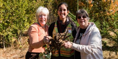 International Corps Member and Volunteer Specialist, Ana Cristina Andre, smiling next to two EarthCorps supporters, and holding up a large root ball.