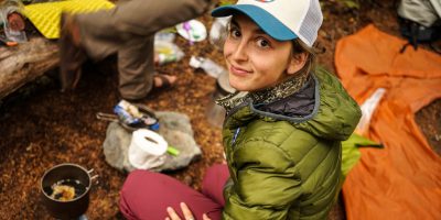 EarthCorps alum, Lindsey Falkenburg kneeling down wearing a hat and coat, and smiling up at the camera.