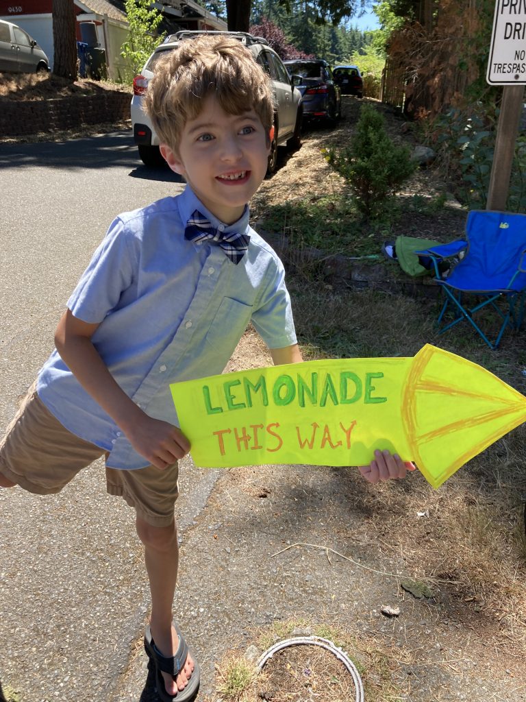Young boy holding an arrow sign that says "lemonade this way"